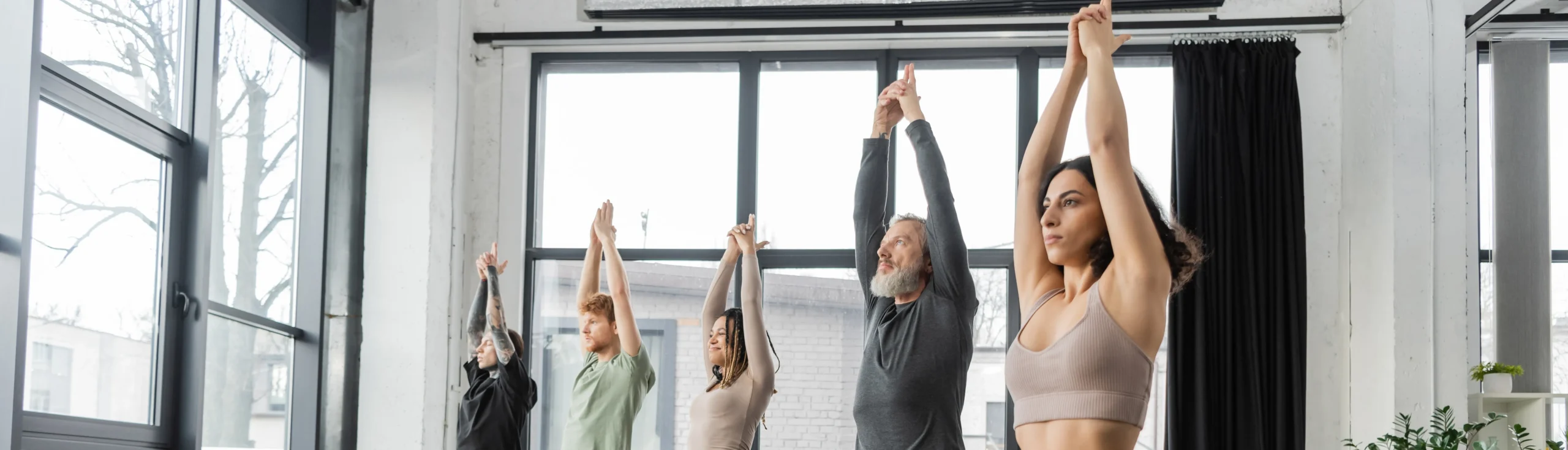 Groupe de cinq personnes, à la diversité de genres, pratiquant un cours de Yoga.