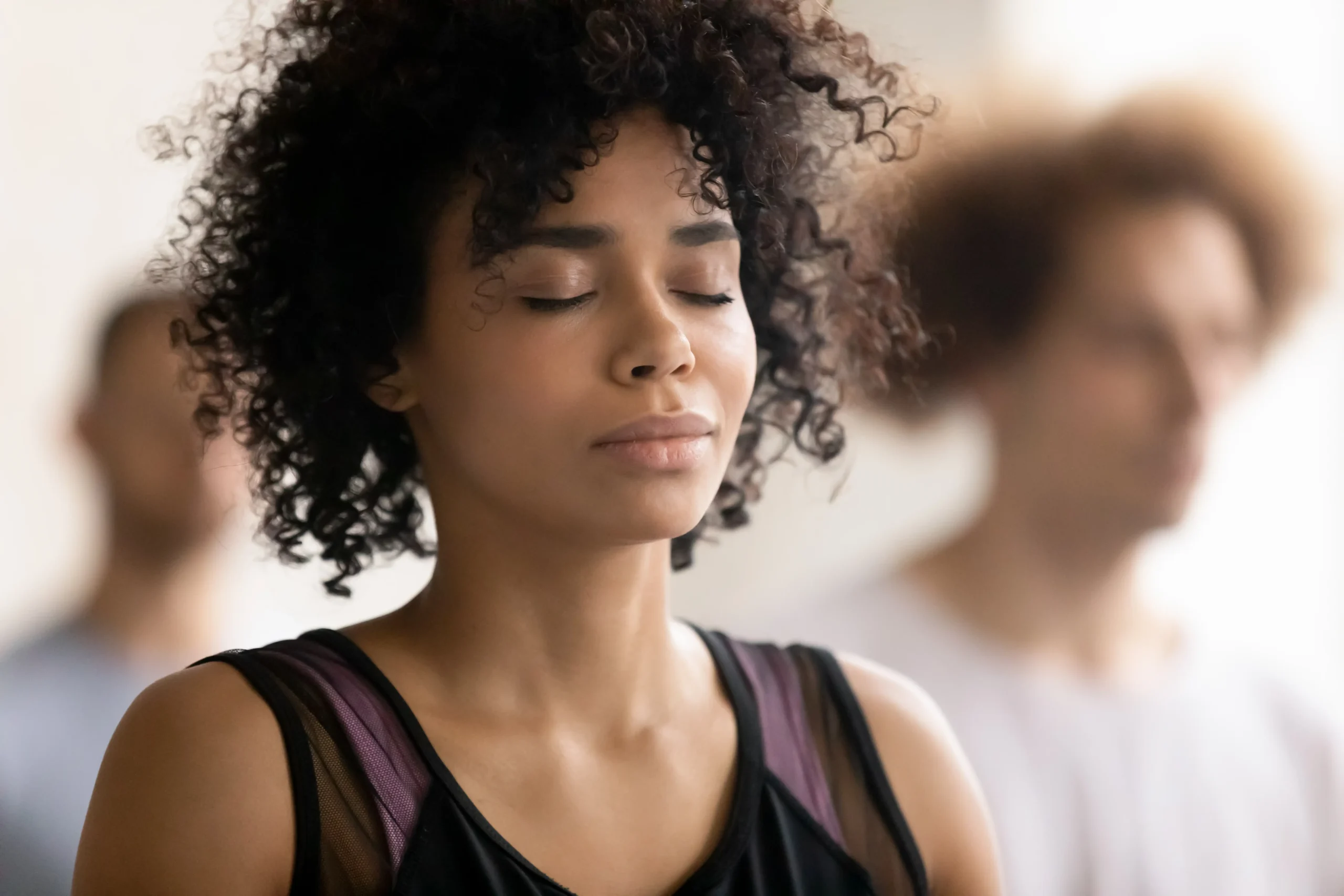 Photo de trois personnes dont une femme afro-américaine sur laquelle est fait la mise au point. La femme a les yeux fermés et semble sereine.